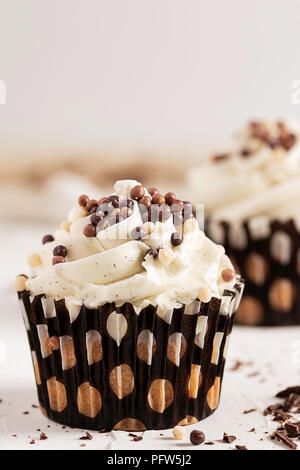 A vanilla cupcake dressed with chocolate balls and another cupcake in soft focus in the background Stock Photo