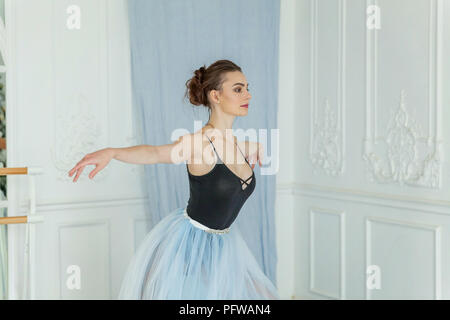 Young classical Ballet dancer side view. Beautiful graceful ballerine practice ballet positions in tutu skirt near large mirror in white light hall. B Stock Photo