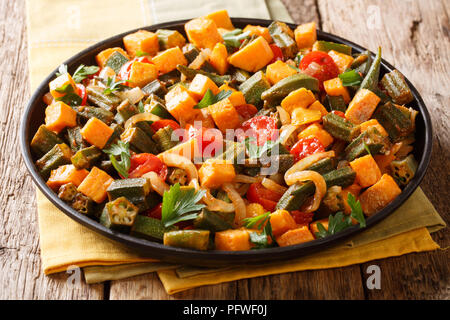 Vegan menu stew of the okra, sweet potato, tomatoes, onions and herbs close-up on a plate on the table. Horizontal Stock Photo