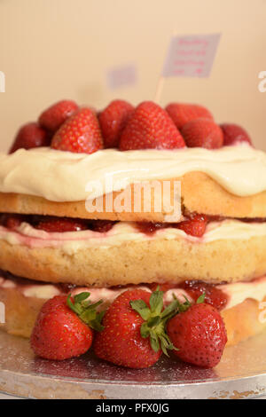 Homemade strawberry and cream sponge layer cake. Juicy red strawberries triple layer cake on a table ready for a birthday party Stock Photo