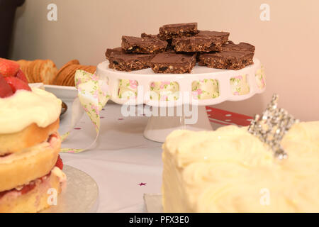 Slices of tiffin chocolate cake biscuit on a cake stand with pretty pink ribbon on a table set up for a birthday party buffet Stock Photo