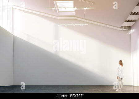 Woman walking near blank white wall mockup in modern gallery with sunrise. Girl admires a clear big stand mock up in museum with contemporary art exhi Stock Photo