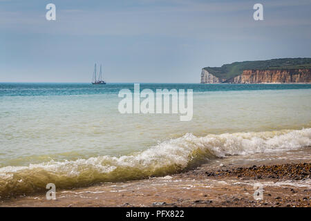 waves on a sandy beach, boat in the sea and britich coast cliffs in the background Stock Photo