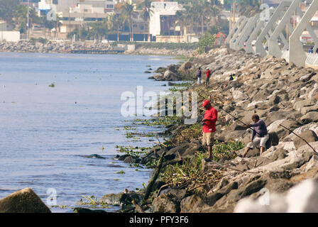 COATZACOALCOS, VER/MEXICO - AUG 18, 2018:  A group of fishermen fishes on the breakwater's rocks at the river mouth Stock Photo