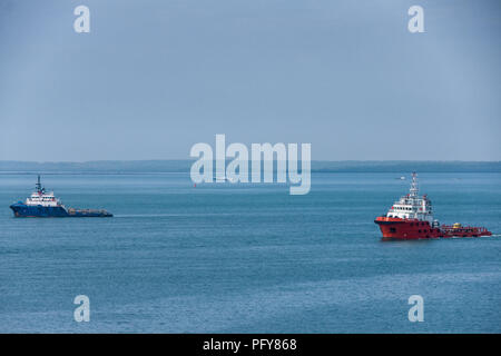 Darwin, Northen Territory, Australia - December 1, 2009: Red and blue tug boats sail in tandem upon blue sea. Faded land line as horizon dividing phot Stock Photo