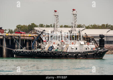 Darwin, Northen Territory, Australia - December 1, 2009: Closeup of two black and white tug boats docked in port under gray sky. Cars onto pier. Stock Photo