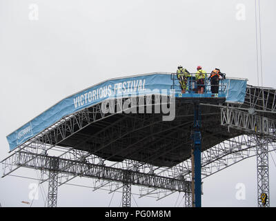 Three workers in a cherry picker assisting in the huilding of a stage for a music festival Stock Photo