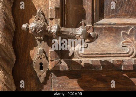 Ornate old worn rusted iron metal door handle and lock with keyhole on decorative carved brown coloured wooden door on sunny day at Kotor, Montenegro. Stock Photo