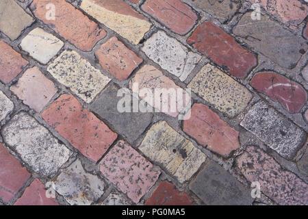 Old smooth worn pink, red and grey coloured rectangular hard stone cobbled paving laid in uniform pattern on road in street at Kotor, Montenegro. Stock Photo