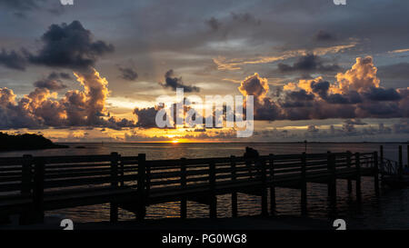 A couple in silhouette (unidentifiable) watches a beautiful Florida Gulf Coast sunset from a pier at Fort Island Beach. Stock Photo