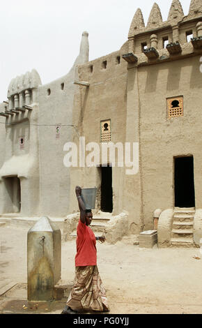 Woman carrying a bucket of water on her head walking past Moroccan and Tukulor houses in Djenne, Mali                FOR EDITORIAL USE ONLY Stock Photo