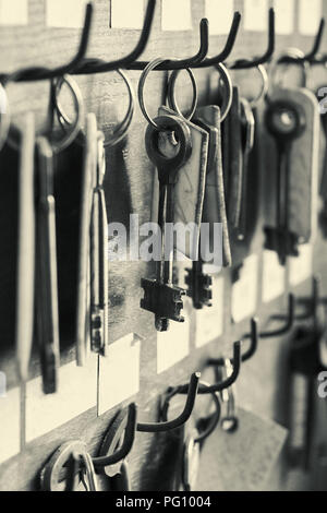 Many old metal keys hanging on the wooden wall with empty labels, black and white cinematic image Stock Photo