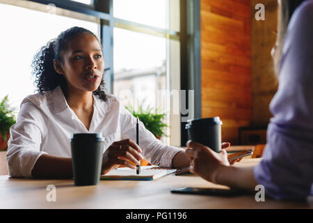 Two managers discussing in cafe. Woman talking with unrecognizable person. Stock Photo
