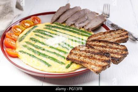 Omelette with asparagus. Homemade ham, cherry tomatoes, toast. Wooden light background Stock Photo