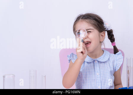 Cute little girl with funny face in school uniform looks through a magnifying glass.Selective focus and and concept image Stock Photo