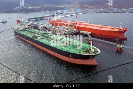 Aerial view of Oil tanker ship loading in port, Crude oil tanker ship under cargo operations on typical shore station with clearly visible mechanical  Stock Photo