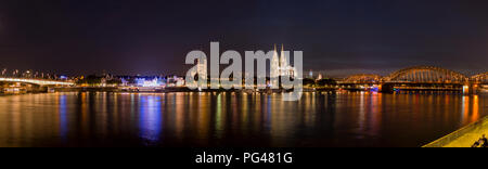 Wide Panorama of Cologne, Germany featuring Cathedral and bridge after sunset at blue hour panorama with river rhine in the foreground Stock Photo