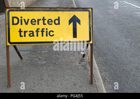 Old, weathered, black and yellow diverted traffic road safety sign on the side of the road. Black text on yellow background with arrow forward Stock Photo