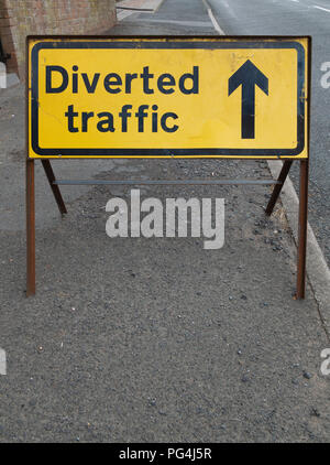 Old, weathered, black and yellow diverted traffic road safety sign on the side of the road. Black text on yellow background with arrow forward Stock Photo