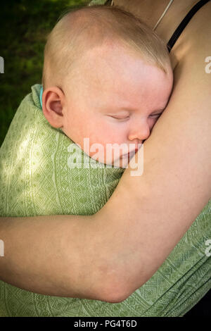 Sleeping baby wrapped in a blanket and held in its mother's arms Stock Photo