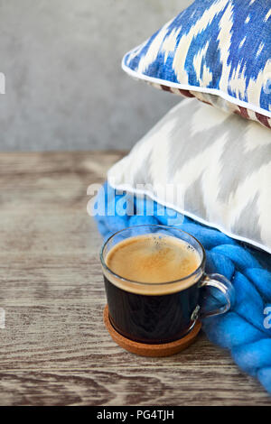 Blue and grey pillows with blanket and cup of coffee on the wooden background. Close up Stock Photo