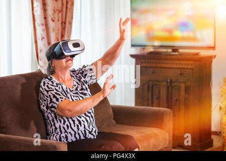 Senior woman with virtual headset or 3d glasses playing videogame at home. Technology, augmented reality, entertainment and people concept. Focus on h Stock Photo