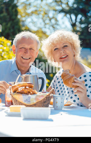 Happy elderly couple eating breakfast in their garden outdoors Stock Photo