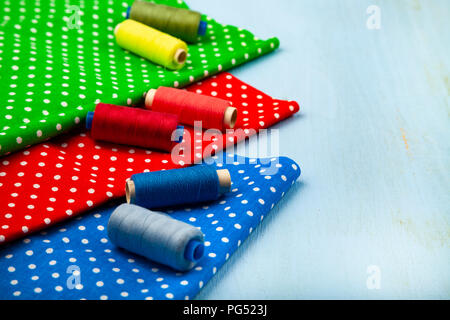 Coils with threads and multi-colored fabrics on a blue wooden background. Fabrics and thread. Stock Photo