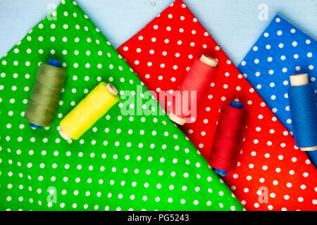 Coils with threads and multi-colored fabrics on a blue wooden background. Fabrics and thread. Stock Photo