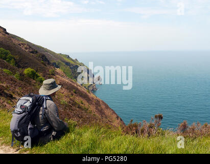 Man Sitting Looking out over the Sea from High Above Heddon's Mouth Beach South West Coastal Path, Devon, England, UK. Stock Photo