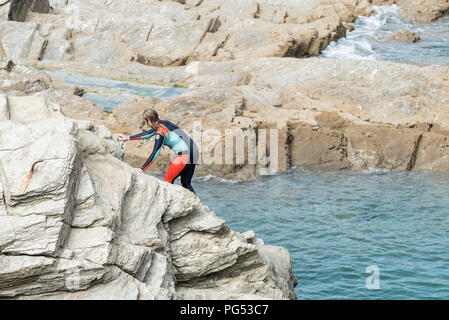 A young teenage girl in a wetsuit climbing on rocks at Little Fistral in Newquay Cornwall. Stock Photo