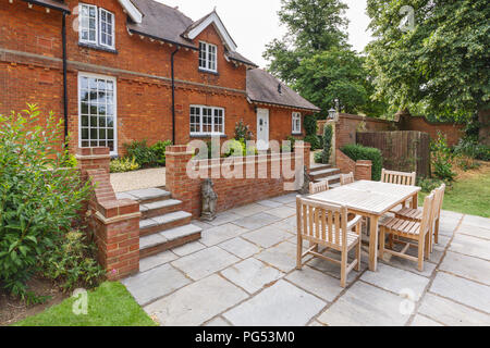 Large historic Victorian house featuring an English garden and patio with wooden furniture. Buckinghamshire, UK
