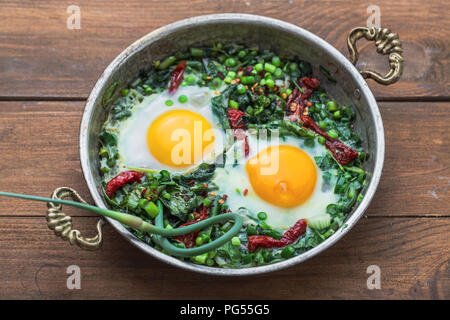 Green shakshuka. Fried eggs with fresh spinach, ramson, leek in a pan on a gray background, top view Stock Photo