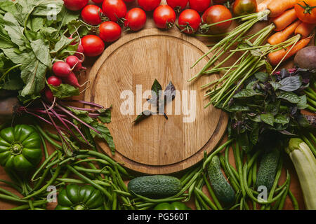 Variety of fresh vegetables and herbs by cutting board on wooden table Stock Photo