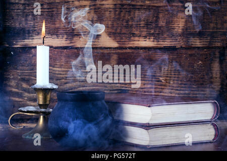 Books of magic and witch pot with smoke and candle burning in candlestick. Old wooden background. Halloween concept. Close up, selective focus Stock Photo