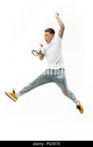 Soccer fan jumping on white background. The young man as football fan with megaphone isolated on orange studio. Support concept. Human emotions, facial expression concepts. Stock Photo