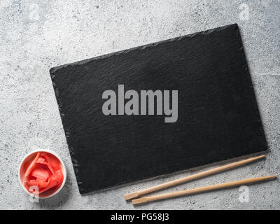 Empty slate plate on gray cement background with chopsticks and pickled ginger. Copy space. Top view or flat-lay. Concept for restaurant and delivery sushi and rolls