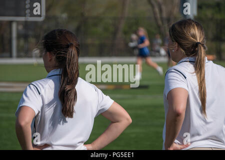 Two female head coaches stand on sidelines calling instructions to girl soccer players in tournament match game on grass field. Over the shoulder blur Stock Photo