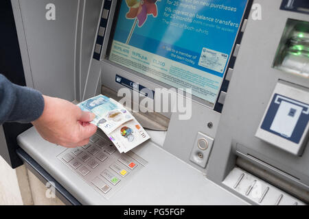 A woman removes £5 and £10 notes from an outside Barclays Bank, hole in the wall, cash point machine Stock Photo