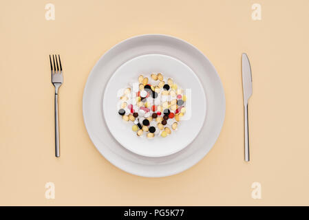 elevated view of fork, knife and plate with various pills on beige background Stock Photo