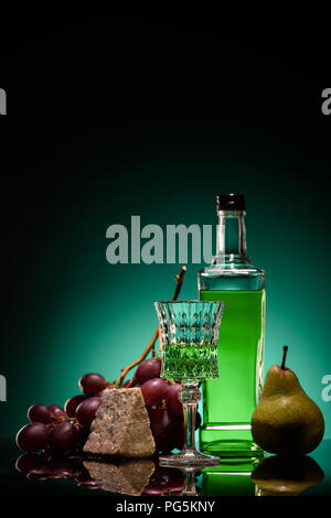 close-up shot of absinthe with fresh pear, grapes and cheese on mirror surface on dark blue background Stock Photo