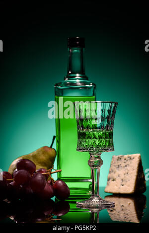 close-up shot of absinthe with fruits and cheese on mirror surface on dark blue background Stock Photo