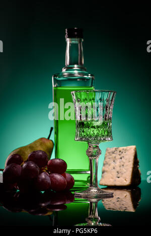 close-up shot of absinthe with ripe fruits and cheese on mirror surface on dark blue background Stock Photo