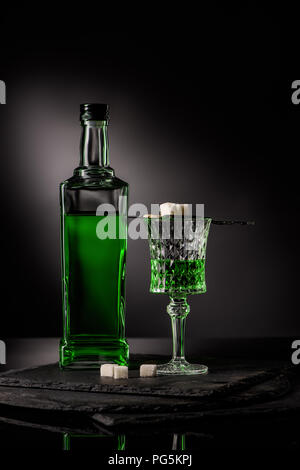 close-up shot of glass and bottle of absinthe with spoon and sugar cubes on dark background Stock Photo