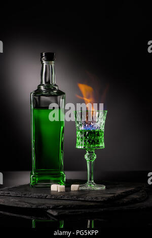 close-up shot of bottle and glass of burning absinthe on dark background Stock Photo