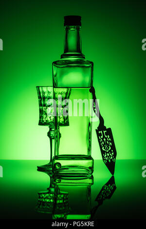 absinthe bottle with crystal glass and spoon on reflective surface and dark green background Stock Photo