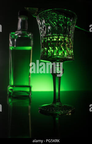 close-up shot of glass with absinthe and bottle on reflective surface and dark green background Stock Photo