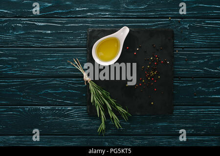 top view of rosemary, oil and pepper corns black stone slate on wooden tabletop Stock Photo