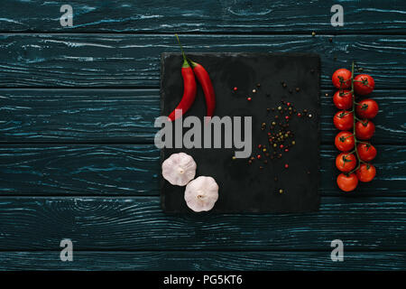 top view of vegetables and chilli peppers on stone cutting board on green wooden tabletop Stock Photo