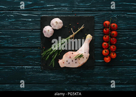 top view of chicken leg with garlic, rosemary, pepper corns and cherry tomatoes on stone board Stock Photo
